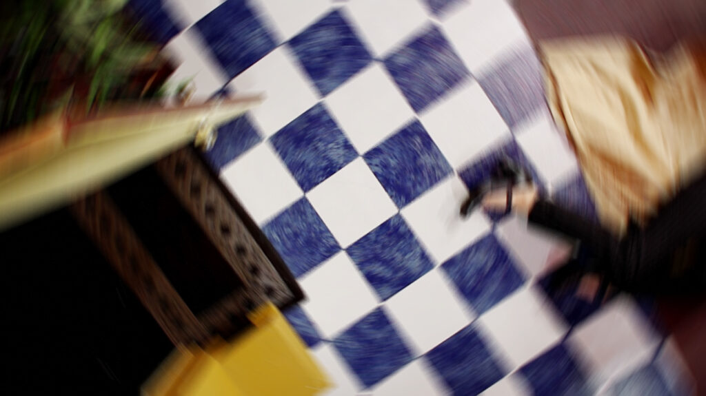 An image of a checkered floor and an open door from above, with a partial view of a woman's body on the floor